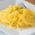 perfectly cooked spaghetti squash on white plate with fork ready to eat